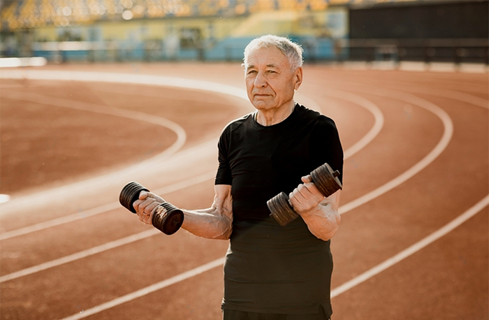 A Stamina for Men close up of an elderly man in black sportswear. Senior man exercising with dumbbells at the stadium. 