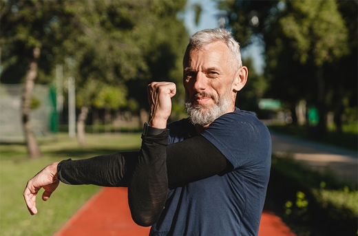 Cropped closeup shot of a male runner athlete stretching his arms before jogging training outdoors in stadium. Flexible sportsman doing workout in park.