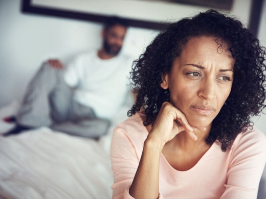 Man suffering from performance anxiety lying on bed with wife looking sad