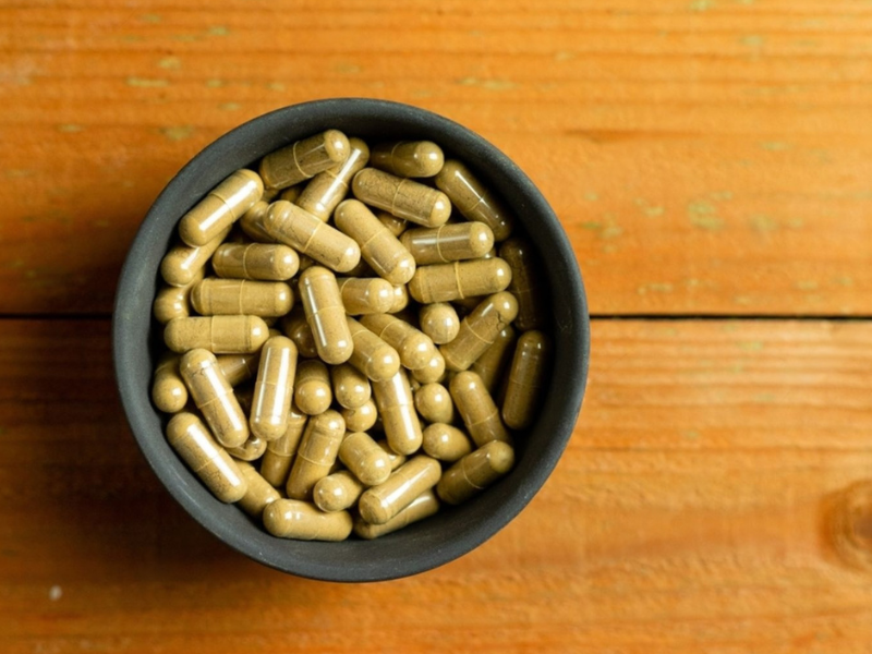 Herbal supplement capsules in a dark bowl on a wooden surface, illustrating how to choose a men's herbal supplement