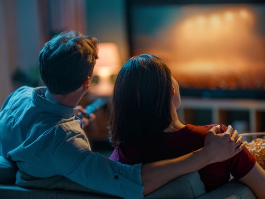Couple relaxing on a sofa at home in warm evening light, watching television together