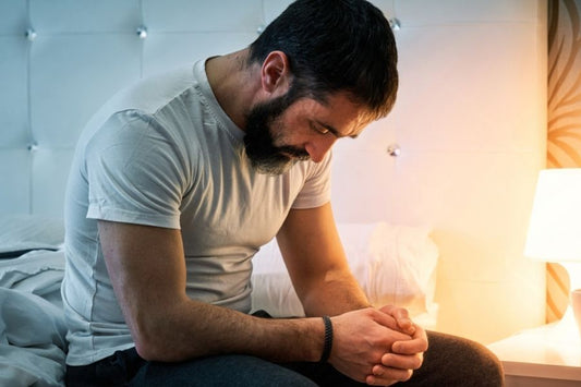 Man sitting alone on the edge of a bed at night, representing sexual performance anxiety