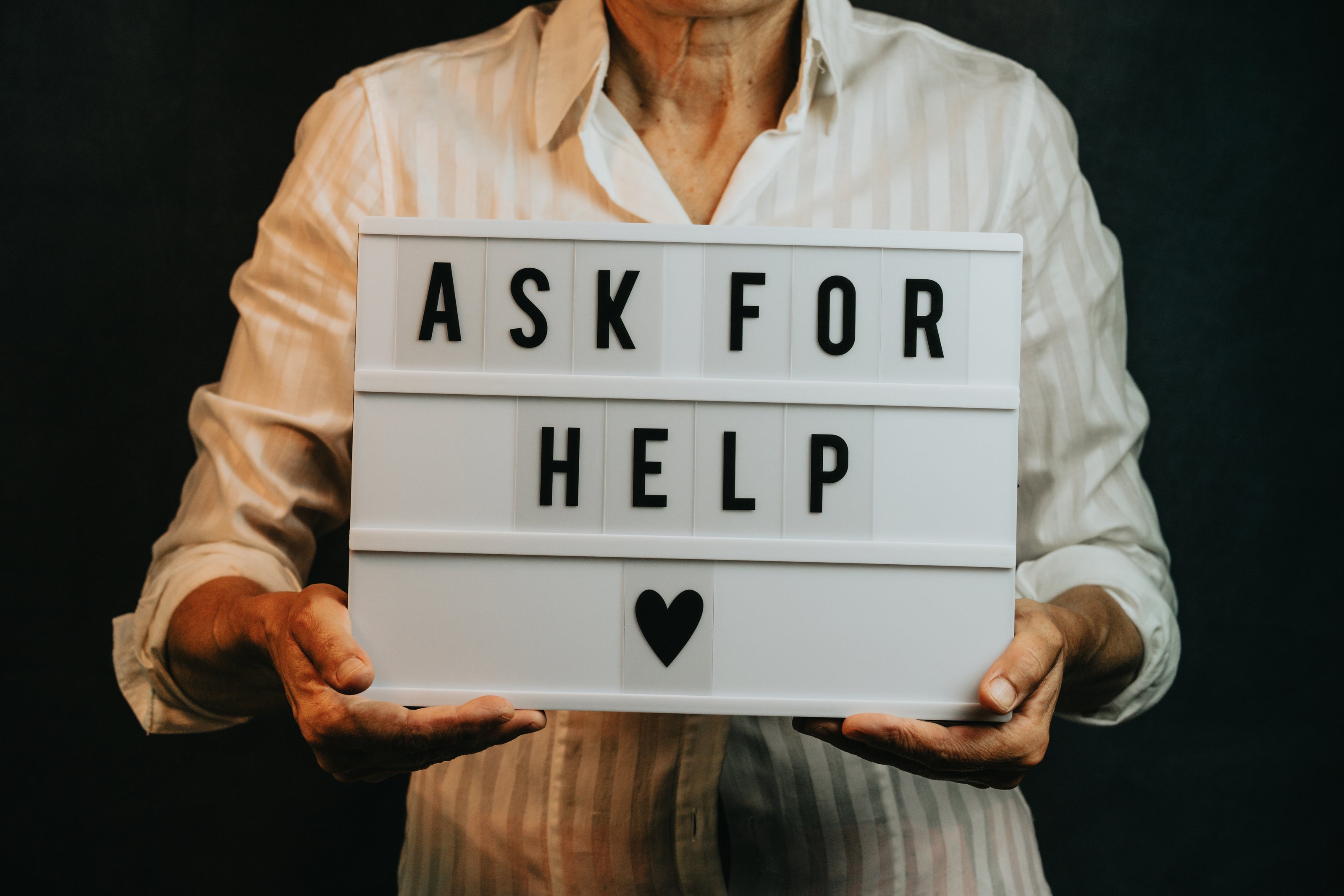 Ask for Help sign being held by man wearing long sleeve shirt